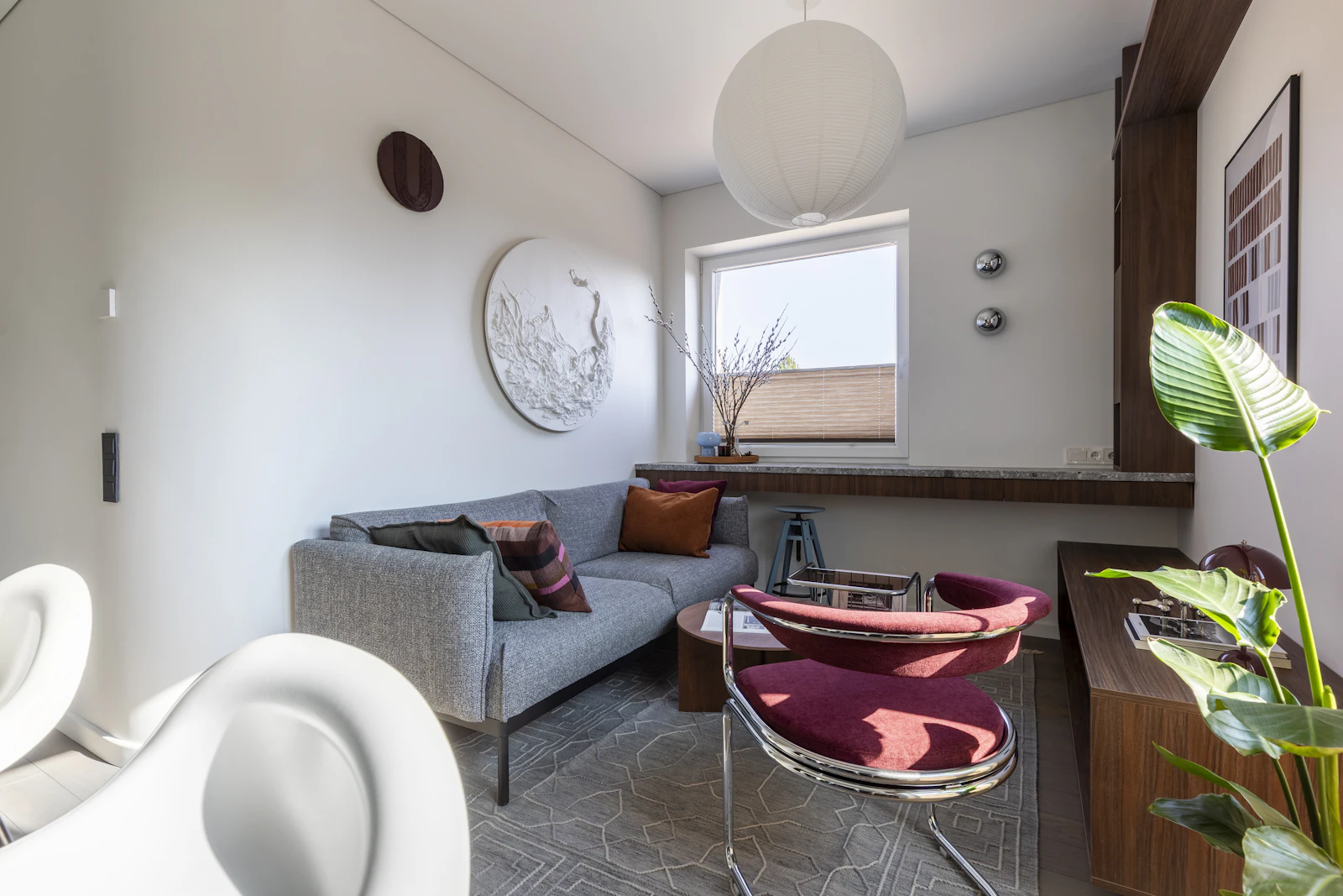 Bright modern small living room with a grey sofa, red armchair, round paper lamp and a plant